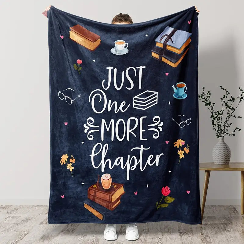 Person holding a dark blue blanket with 'Just One More Chapter' text and book illustrations.