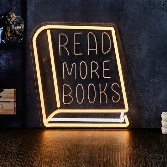 Neon sign shaped like an open book with 'READ MORE BOOKS' text on a dark background.