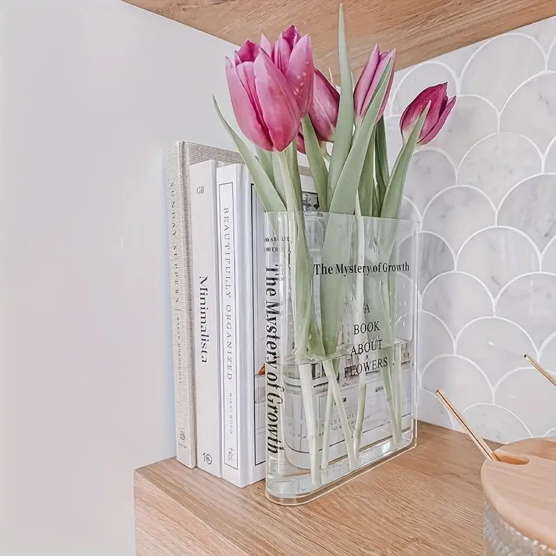 Clear vase with pink tulips on a stack of books against a marble wall.